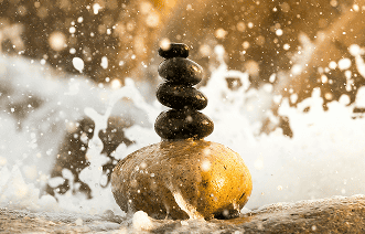 Stacked stones balancing on a smooth rock in a flowing water setting, symbolizing relaxation and balance.